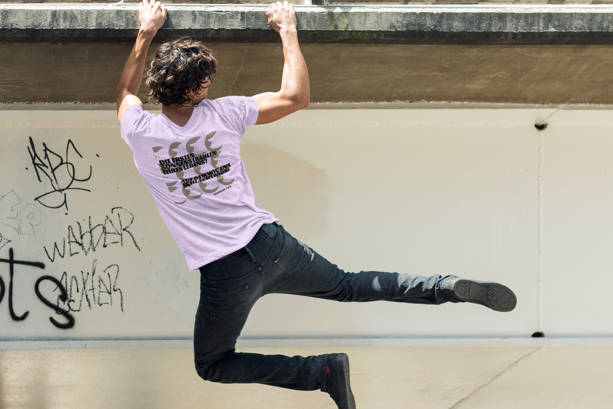 Person, die sich mit seinen Händen an einem Mauervorsprung festhält. Auf dem lilafarbenen T-Shirt sind Schweineköpfe aufgedruckt und der Schriftzug lautet: "Die ersten Sonnenstrahlen ihres Lebens -auf dem Weg ins Schlachthaus."