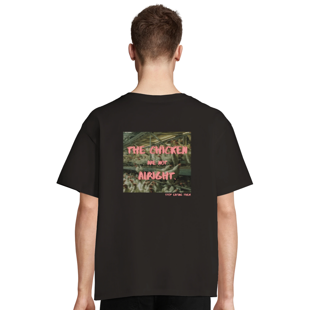 Person trägt schwarzes T-Shirt oversized mit dem Backprint: "The chicken are not alright. Stop eating them." Im Hintergrund des Schriftzugs ist ein Bild von Hühnern, zusammengedrängt auf engem Raum.