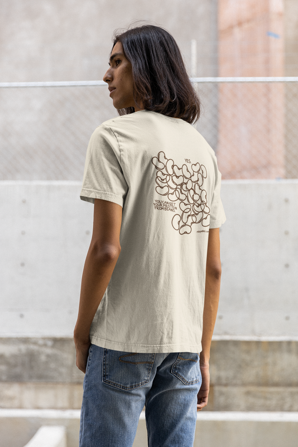 Mann mit schulterlangen braunen Haaren, der ein beiges T-Shirt trägt mit mehreren aufgedruckten Bohnen und dem Spruch: "Yes, you can get your protein from beans."