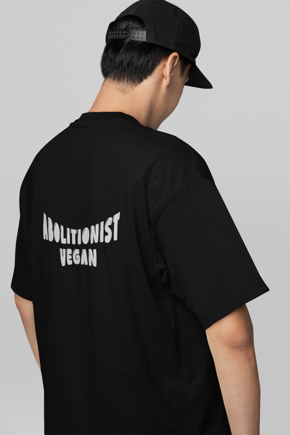 Mann mit einer schwarzen Cap und einem schwarzen, oversized T-Shirt mit dem Aufdruck: Abolitionist Vegan"